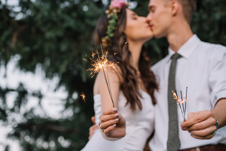 close-up view of happy wedding couple holding sparklers and kissing, selective focusの写真素材