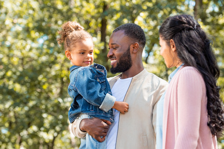 portrait of happy african american parents and daughter standing together in park