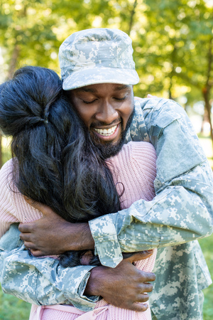 smiling african american soldier in military uniform cuddling girlfriend in parkの写真素材