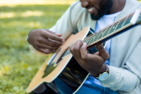cropped image of african american man playing acoustic guitar in park
