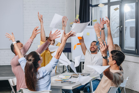 happy businesspeople throwing up documents during meeting in office