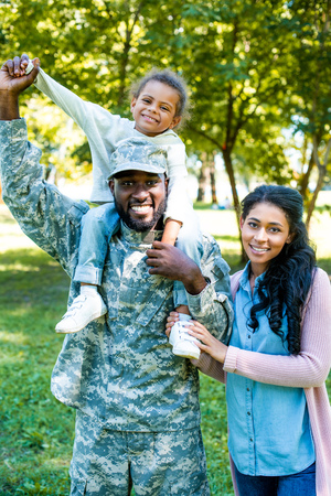 smiling african american soldier in military uniform holding daughter on shoulders in parkの写真素材