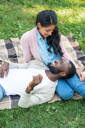 high angle view of happy african american boyfriend lying on girlfriend legs in parkの写真素材