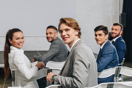 smiling businesspeople sitting on chairs at training in hub and looking at cameraの写真素材