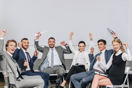 happy businesspeople with raised hands sitting on chairs at training in hubの写真素材
