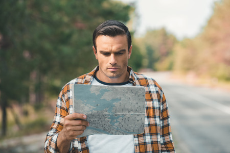 portrait of concentrated tourist looking at map while standing on road