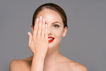 obscured view of attractive young woman with red lipstick on half of mouth isolated on greyの写真素材