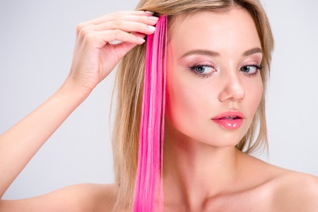 attractive young woman applying pink clip-on hair strand isolated on greyの写真素材