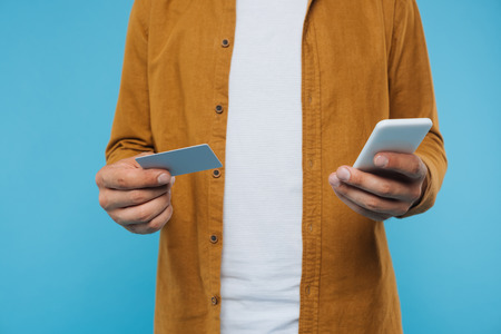 cropped image of man holding credit card and smartphone isolated on blue