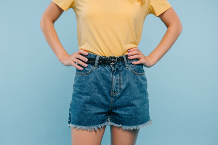 cropped image of girl in shirt and shorts standing with hands akimbo isolated on blueの写真素材