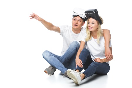 couple sitting with virtual reality headsets and looking away isolated on white