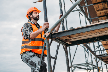 bearded builder climbing on scaffolding at construction siteの写真素材
