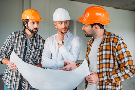 group of handsome architects with blueprint having conversation inside of constructing building
