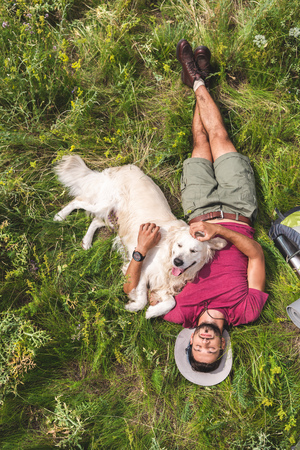 top view of tourist and golden retriever dog lying on green grassの写真素材