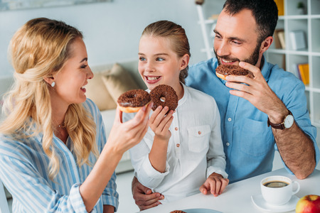 happy young family eating chocolate glazed donutsの写真素材