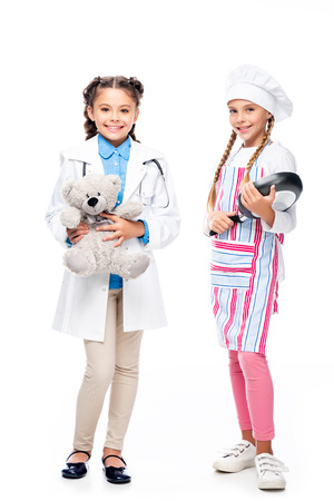 schoolchildren in costumes of doctor and chef standing with teddy bear and frying pan isolated on whiteの写真素材