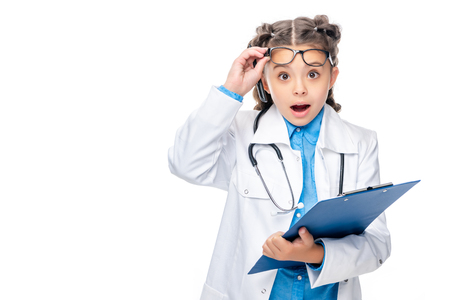 shocked schoolchild in costume of doctor holding clipboard isolated on whiteの写真素材