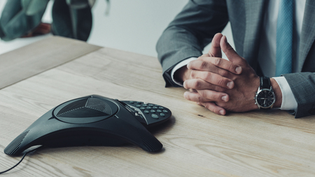 cropped shot of businessman sitting at workplace with conference phoneの写真素材