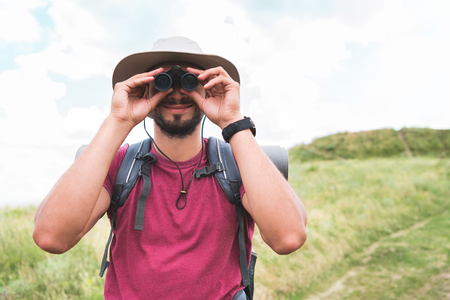 male tourist in hat with backpack looking in binocularsの写真素材