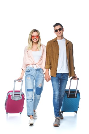 young happy couple holding hands and walking with suitcases isolated on whiteの写真素材
