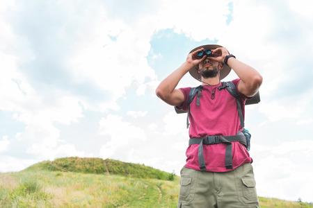 male traveler in hat with backpack looking in binoculars