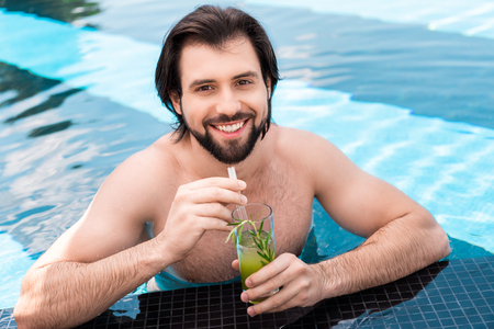 handsome bearded man with glass of cocktail in swimming poolの写真素材