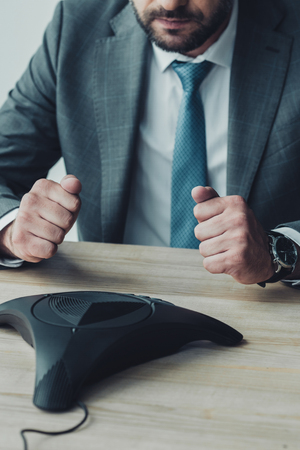 cropped shot of failed businessman sitting in front of conference phone and making fists at officeの写真素材