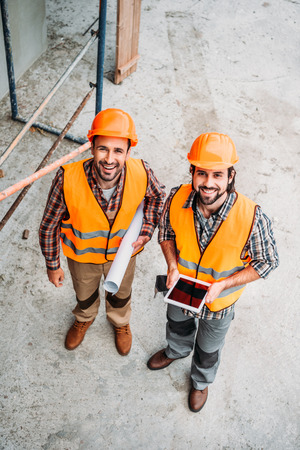 high angle view of builders with blueprint and tablet standing at construction site and looking at cameraの写真素材