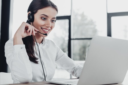 beautiful female call center worker with headphones and laptop sitting at workplaceの写真素材