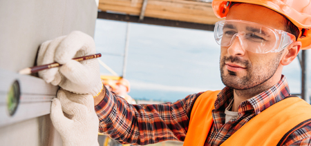 wide shot of handsome builder using bubble level at construction site