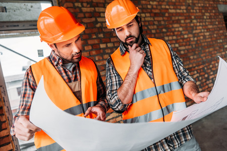 thoughtful confident builders working with blueprint at construction site
