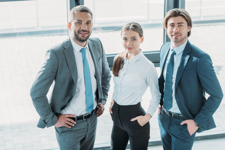 group of smiling young business people standing at modern office and looking at camera