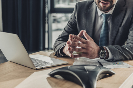 cropped shot of smiling businessman with laptop and contract using speakerphone at officeの写真素材