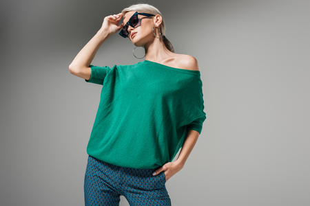 beautiful female model in sunglasses and green sweater posing isolated on grey backgroundの写真素材