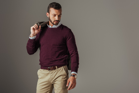 stylish handsome man posing in burgundy sweater with jacket on shoulder, isolated on greyの写真素材
