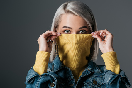 shocked woman in yellow turtleneck and jeans jacket, isolated on grey