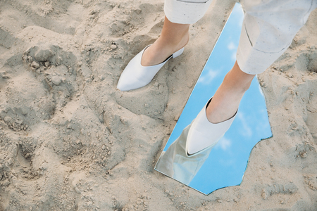 partial view of model standing on sand and piece of mirror with reflection of blue skyの写真素材