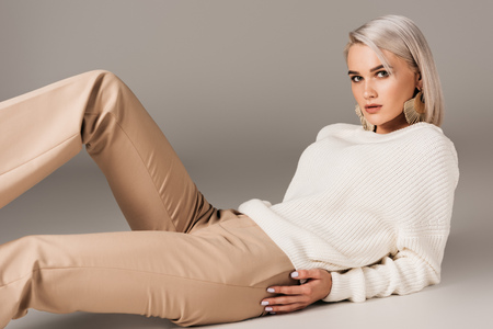 elegant blonde woman lying in white sweater and beige pants, on greyの写真素材