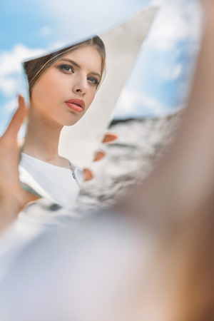 beautiful stylish girl holding piece of mirror and looking on her reflectionの写真素材