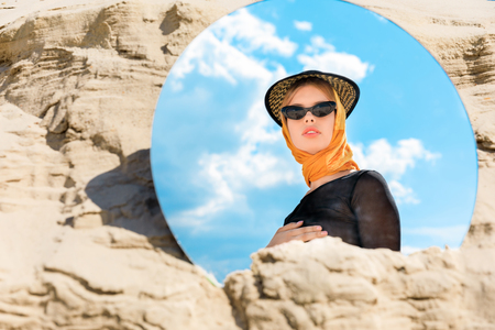 round mirror with reflection of beautiful stylish model in hat and sunglassesの写真素材