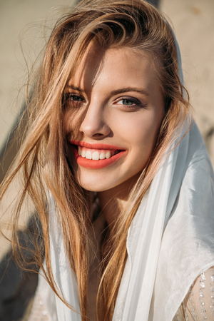 attractive blonde cheerful girl in white silk scarf looking at cameraの写真素材