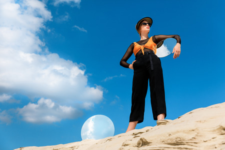 elegant beautiful model in stylish clothes posing with round mirrors with reflection of cloudy skyの写真素材