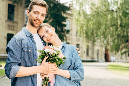happy young couple holding flower bouquet at park and looking at cameraの写真素材