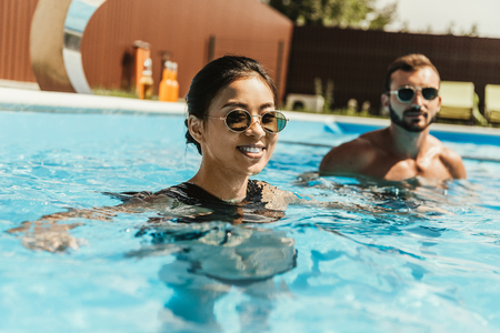 attractive asian girl in swimming pool with boyfriend behindの写真素材