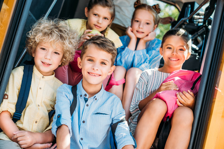 group of smiling schoolchildren sitting on stairs of school bus and looking at camera
