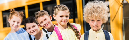 panoramic shot of group of adorable pupils looking at camera while standing in row in front of...