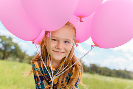 portrait of cute child with pink balloons looking at camera in summer fieldの写真素材