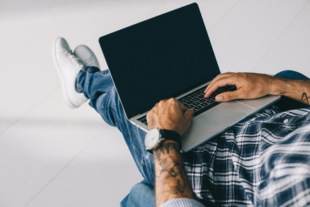 cropped view of tattooed man typing on laptop with blank screenの写真素材