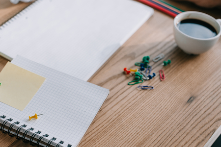 close up of notebooks, paper clips and cup of coffee on wooden table