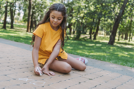 beautiful child sitting and drawing with chalk in parkの写真素材